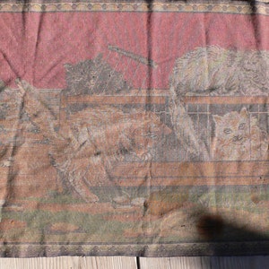 May include: A vintage tapestry wall hanging with a red background and a scene of cats in a barn. The tapestry is woven with brown, white, and black threads.