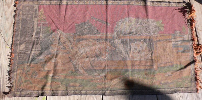 May include: A vintage tapestry wall hanging with a red background and a scene of cats in a barn. The tapestry is woven with brown, white, and black threads.