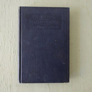 May include: A dark blue hardcover book with the title "Printing and the Allied Trades" by R. Randolph Karch.