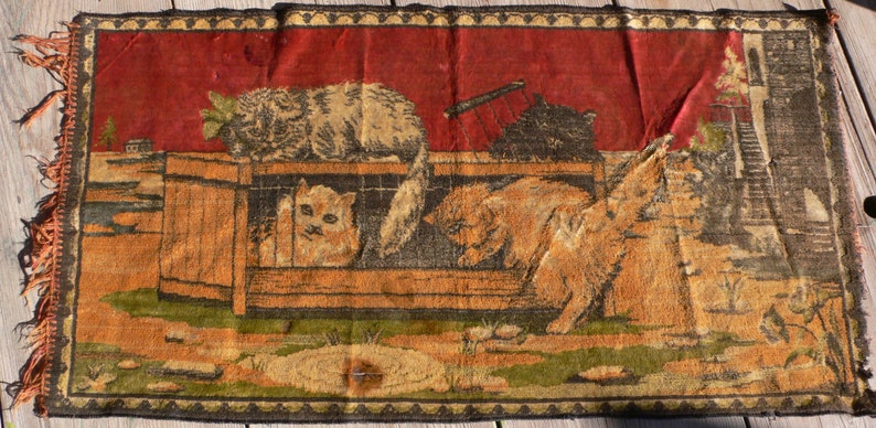 May include: A vintage tapestry rug with a red background featuring a scene of cats in a cage. The cats are brown, white, and black. The rug has a fringe border and is woven with intricate details.