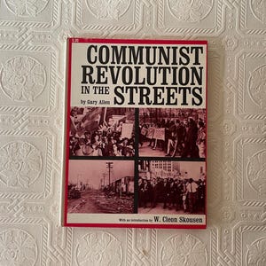 Puede incluir: Un libro titulado "COMMUNIST REVOLUTION IN THE STREETS" de Gary Allen. La portada tiene un borde rojo y texto negro. El libro incluye im&aacute;genes de multitudes y escenas callejeras. El precio de 5,00 es visible en la esquina superior izquierda.