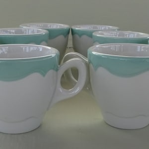 May include: Set of eight white ceramic coffee mugs with a light blue rim. The mugs are all the same size and shape.