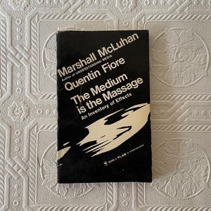 May include: A vintage paperback book titled "The Medium is the Massage" by Marshall McLuhan and Quentin Fiore. The cover is black with white text and a white abstract design. The book is a Bantam Book.