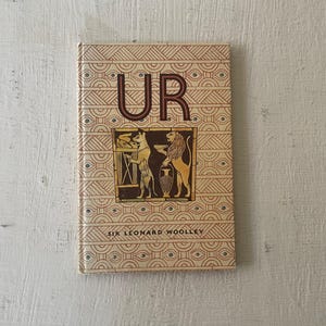 May include: A vintage book titled "UR" by Sir Leonard Woolley. The cover features a geometric pattern in shades of red, brown, and blue, with a central illustration of a lion and a dog.