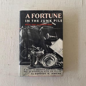Puede incluir: Una portada de libro en blanco y negro con el título "A Fortune in the Junk Pile" y el texto "Over 300 Illustrations". La portada presenta una foto de objetos antiguos, incluyendo una jarra de plata, un tazón de plata y una bandeja de plata.