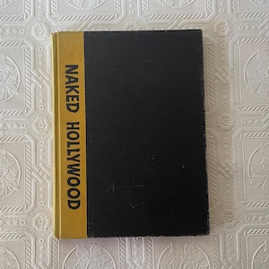 May include: A hardcover book titled "Naked Hollywood." The book has a black cover with a yellow spine. The title is printed vertically in bold, white letters on the spine.