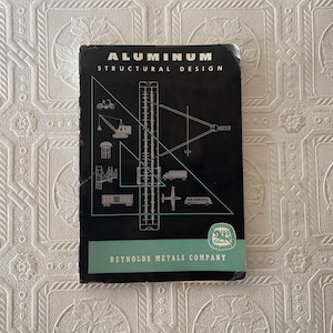 May include: A vintage book titled "ALUMINUM STRUCTURAL DESIGN" with illustrations of construction equipment and vehicles. The cover is black with white text and a teal stripe at the bottom. The Reynolds Metals Company logo is visible.
