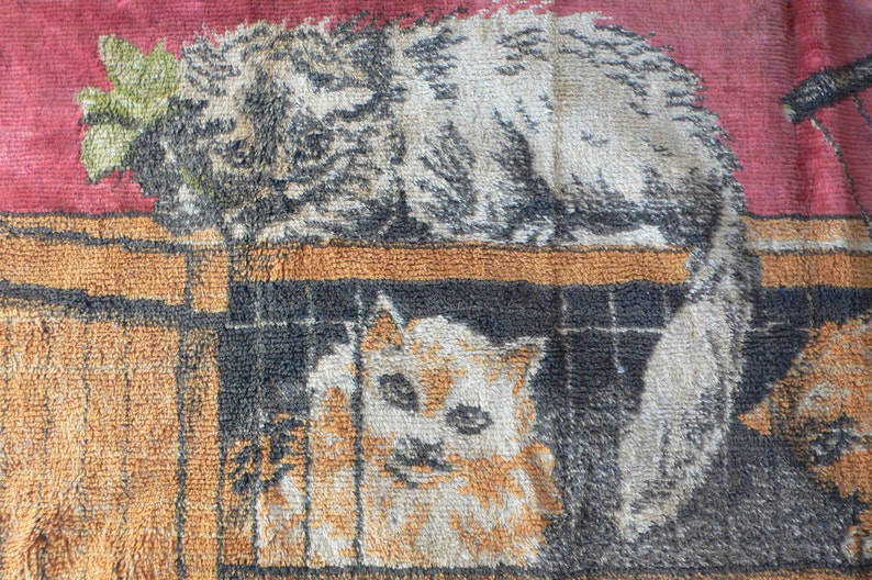 May include: A vintage tapestry featuring two cats, one with a green leafy branch behind it, and the other in a cage. The tapestry has a brown, orange, and red color scheme.