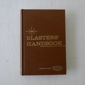 May include: A brown book titled "Blasters' Handbook" with a gold star design and the text "fifteenth edition" and "DuPont" on the cover.