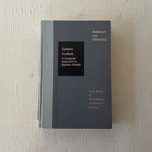 May include: A hardcover book titled "Systems Analysis: A Computer Approach to Decision Models" by McMillan and Gonzalez. The book has a gray cover with black text and is part of the Irwin Series in Quantitative Analysis for Business.