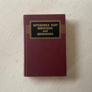 May include: A burgundy hardcover book with gold lettering on the spine and front cover. The title is "Automobile Body Rebuilding and Refinishing".