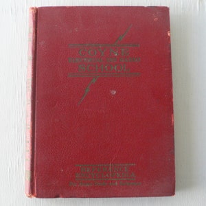 May include: A red hardcover book with the title "COYNE ELECTRICAL SCHOOL" in gold lettering. The book has a lightning bolt design on the cover.