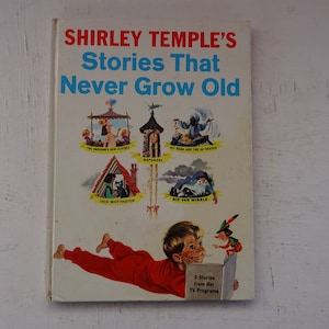 May include: A vintage book cover featuring Shirley Temple's Stories That Never Grow Old. The cover features a young boy in red pajamas reading a book with a fairy tale character. The book cover also features illustrations of five classic fairy tales: The Emperor's New Clothes, Rapunzel, Ali Baba and the 40 Thieves, Dick Whittington, and Rip Van Winkle.