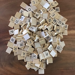 May include: A pile of wooden letter tiles for a Scrabble game. The tiles are in various letters and numbers, including the blank tile.