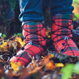 May include: Red and brown plaid boots with black laces and a drawstring closure. The boots are worn outdoors, surrounded by fallen leaves. The boots have a green plaid cuff.
