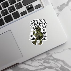 May include: A sticker featuring a cartoon turtle in military gear with the text "SHELL YEAH". The turtle is wearing sunglasses and giving a thumbs-up, with palm trees and a sun in the background.