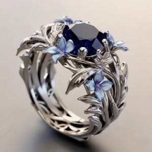 以下が含まれることがあります： 中央に大きな濃い青色の宝石をあしらったシルバーリング。リングは、ピンク色の中心を持つ小さな青い花など、繊細な花と葉のディテールで飾られています。デザインは複雑で、詳細です。