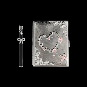 K&ouml;nnte beinhalten: Eine silberne Zigarettenetui und ein passendes Feuerzeug. Die Etui hat ein eingraviertes Blumenmuster mit herzf&ouml;rmigem Ausschnitt und rosa Edelsteinakzenten. Das Feuerzeug ist schwarz mit einer Schleife.