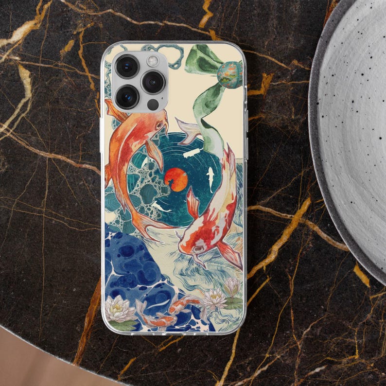 May include: Clear phone case featuring a koi fish design. The artwork depicts two orange and white koi fish swimming around a teal circle with a red sun. The background includes blue water, white flowers, and a green ribbon.
