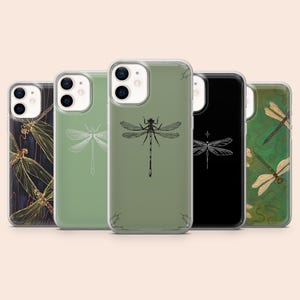 May include: Five smartphone cases arranged in a row, featuring various dragonfly designs. The cases include a dark background with gold dragonflies, a sage green case with a white outline, a sage green case with a black dragonfly, a black case with a white dragonfly, and a green patterned case with detailed dragonflies.