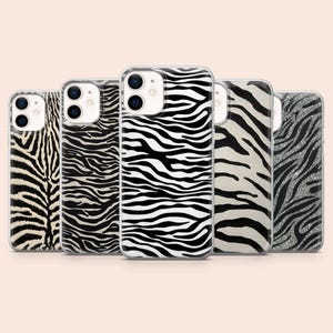 Può includere: Cinque custodie per telefono con motivi zebrati. Le custodie presentano motivi in bianco e nero, alcune con finitura argento glitterata. Le custodie sono disposte in fila, mostrando la varietà dei design.