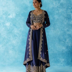 May include: A navy blue three-piece outfit, comprising a crop top, palazzo trousers, and a long jacket, embellished with gold embroidery. The ensemble is set against a light blue background. The text "RIWAAYAT SHOP" is visible.