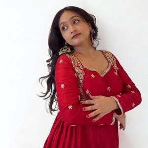 May include: A red dress with gold embroidery and long sleeves. The dress has a V-neckline and is adorned with gold embellishments. The text "RIWAAYAT SHOP" is visible in the upper right corner.