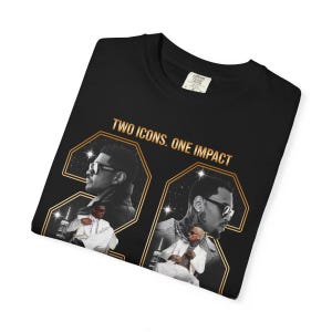 May include: A black t-shirt featuring a graphic print with the text "TWO ICONS. ONE IMPACT" in gold lettering. The design includes two large gold-outlined numbers and photographic portraits of two individuals wearing sunglasses and white suits.