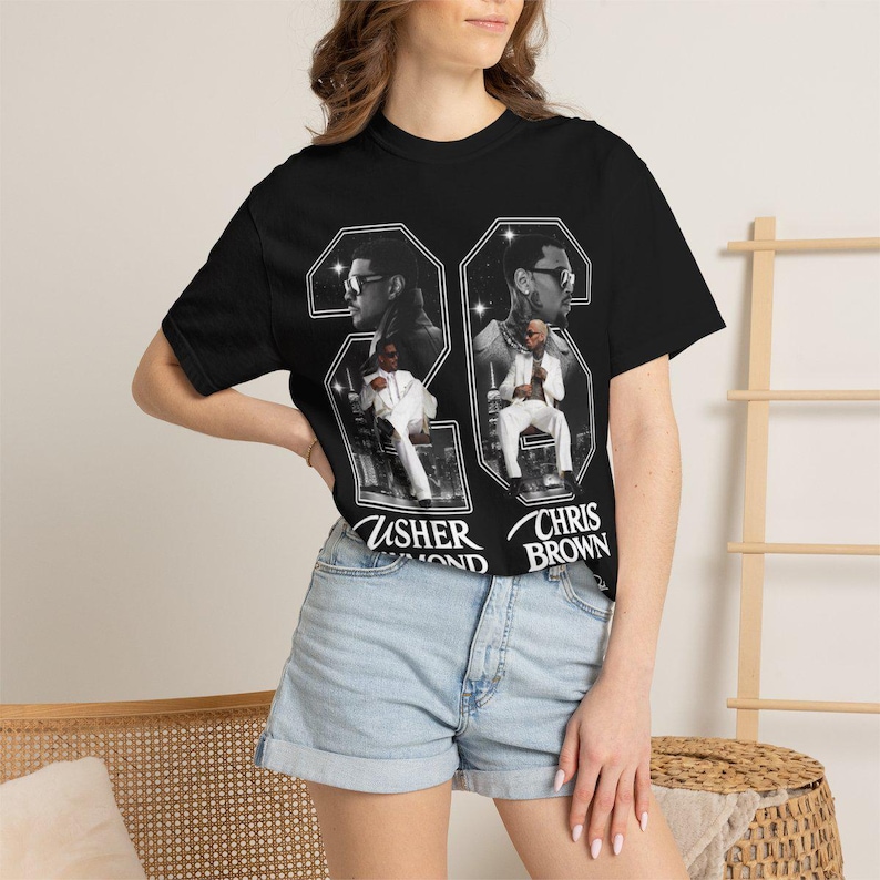 May include: A black short-sleeve t-shirt featuring a large graphic print of Usher Raymond and Chris Brown. The design includes the number 23, black and white portraits, and full-body images of both artists in white suits with their names printed below.