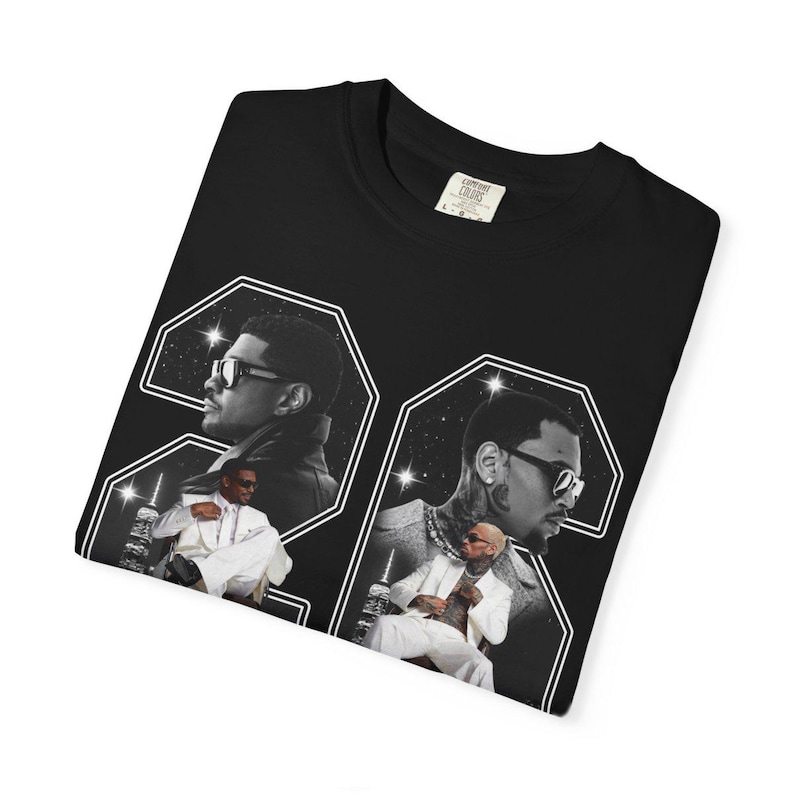 May include: A black t-shirt featuring a large graphic print of the number 24. Inside the digits are black and white photographic portraits of a person wearing sunglasses and a white suit, set against a starry night sky and city skyline background.