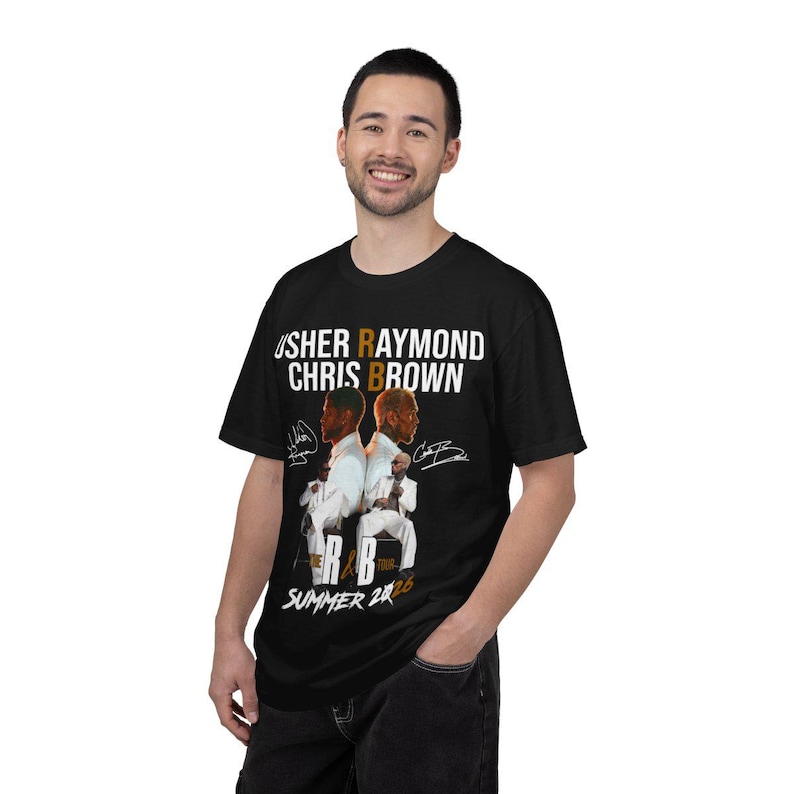 May include: A black t-shirt featuring a graphic print of Usher Raymond and Chris Brown in white suits. The text reads USHER RAYMOND CHRIS BROWN, THE R&B TOUR, and SUMMER 2026, accompanied by two signatures on either side of the central figures.