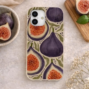 May include: A clear phone case featuring a fig design. The case has a repeating pattern of whole and sliced figs in shades of purple, orange, and green. The background is a light beige color. The phone case is on a light-colored surface.