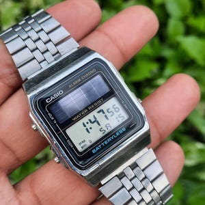 May include: A silver Casio digital watch with a black face displaying the time 1:47:56. The watch has a rectangular face with the words "ALARM CHRONO" and "WATER RESIST". The watch band is made of silver metal links.