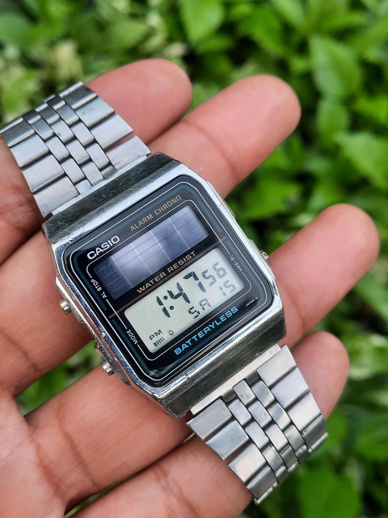 May include: A silver Casio digital watch with a black face displaying the time 1:47:56. The watch has a rectangular face with the words "ALARM CHRONO" and "WATER RESIST". The watch band is made of silver metal links.
