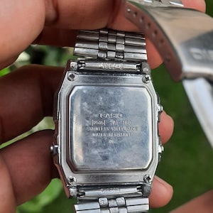 May include: A stainless steel Casio digital watch, viewed from the back. The watch face displays the brand name, model number, and text indicating a stainless steel back and water resistance. The watch band is a silver, linked design.