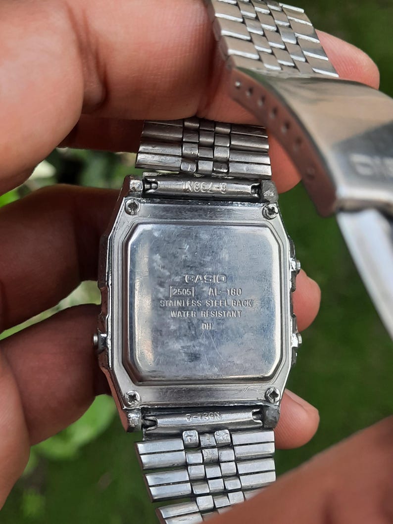 May include: A stainless steel Casio digital watch, viewed from the back. The watch face displays the brand name, model number, and text indicating a stainless steel back and water resistance. The watch band is a silver, linked design.