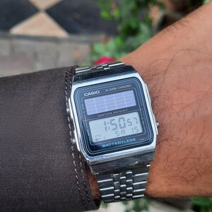May include: A silver Casio digital watch with a rectangular face and a metal band. The watch displays the time as 1:50:57 PM and the date as SA 15. The watch face includes the text "CASIO", "ALARM CHRONO", "WATER RESIST", and "BATTERYLESS".