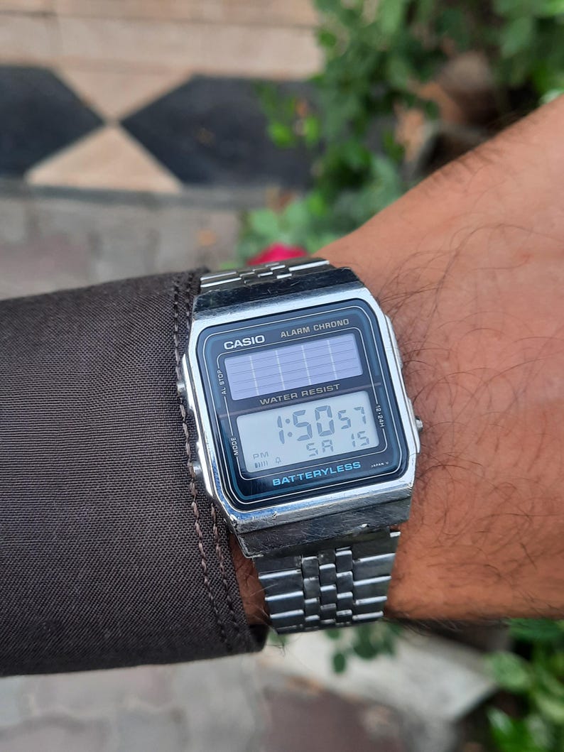 May include: A silver Casio digital watch with a rectangular face and a metal band. The watch displays the time as 1:50:57 PM and the date as SA 15. The watch face includes the text "CASIO", "ALARM CHRONO", "WATER RESIST", and "BATTERYLESS".