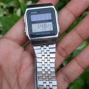 May include: A silver Casio digital watch with a black face displaying the time 1:48:25. The watch has a rectangular face with the words "CASIO" and "ALARM CHRONO" printed on it. The watch band is made of silver metal.