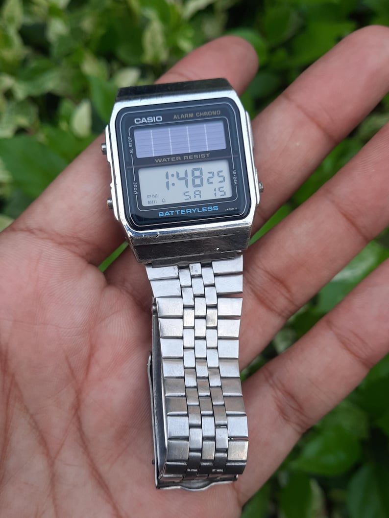 May include: A silver Casio digital watch with a black face displaying the time 1:48:25. The watch has a rectangular face with the words "CASIO" and "ALARM CHRONO" printed on it. The watch band is made of silver metal.