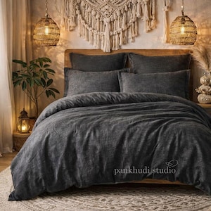 May include: A charcoal grey bed set, including a duvet cover and pillowcases, on a wooden bed frame. A macrame wall hanging is above the bed. Woven pendant lights hang either side of the bed, creating a warm, inviting atmosphere.