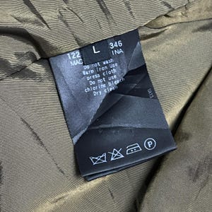 May include: A close-up of a clothing tag with care instructions. The tag is black with white text, including "Do not wash", "Dry clean", and other symbols. The tag is inside a garment with a brown lining.