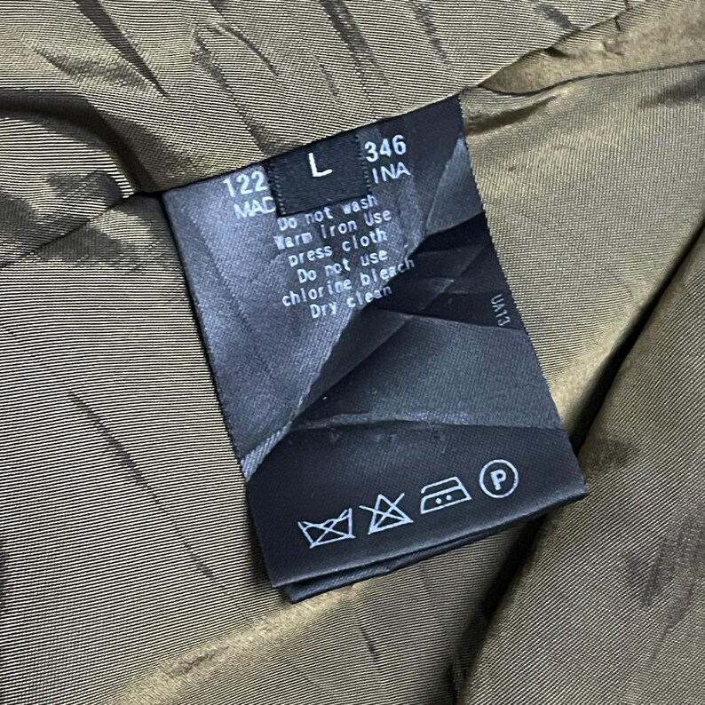 May include: A close-up of a clothing tag with care instructions. The tag is black with white text, including "Do not wash", "Dry clean", and other symbols. The tag is inside a garment with a brown lining.