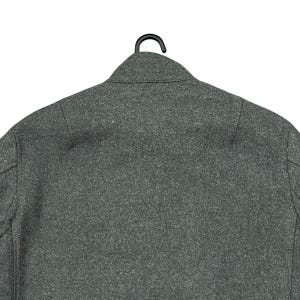 May include: A gray wool coat, viewed from the back, hanging on a black hanger. The coat has a classic collar and a tailored fit. The fabric has a textured appearance.