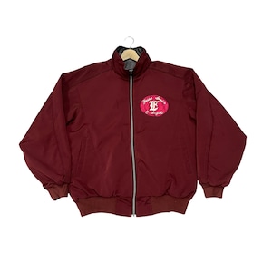 Op de afbeelding: Bordeauxkleurige bomberjack met een ritssluiting over de hele lengte en een hoge kraag. De jas heeft een bordeauxrode en witte geborduurde patch op de borst met de tekst "Jesse James O. Angels". De jas heeft bordeauxrode geribde manchetten en zoom.