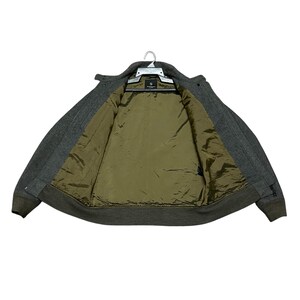 May include: A gray wool jacket with a dark olive green interior lining, hanging on a white hanger. The jacket has a button-up front and a ribbed hem and cuffs. The jacket is open, revealing the interior lining.