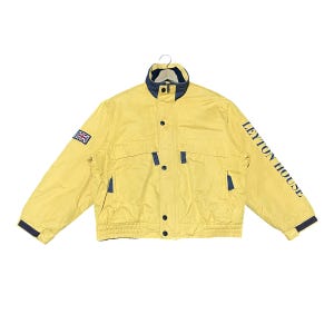 May include: A yellow jacket with a high collar, featuring dark blue accents on the collar, cuffs, and pocket trim. The text LEYTON HOUSE is printed in dark blue on the left sleeve, and a small Union Jack flag patch is on the right sleeve.