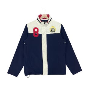 May include: A navy blue and cream color-blocked jacket featuring a high collar with a red interior lining. The front displays a large red number 8 on the right chest and a circular crest logo on the left chest. It has a full-length center zipper.