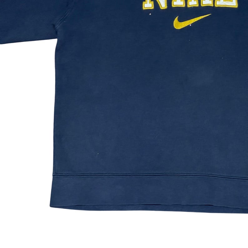 Puede incluir: Sudadera azul marino con la palabra "NIKE" en letras amarillas y un logotipo de swoosh amarillo. La sudadera tiene un dobladillo acanalado y cuello redondo. La tela parece ser un material suave y c&oacute;modo.
