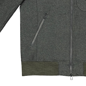 May include: Close-up of a dark gray zip-up jacket with a diagonal zippered pocket on the left side. The jacket has a dark green ribbed hem and cuffs. The zipper is silver.